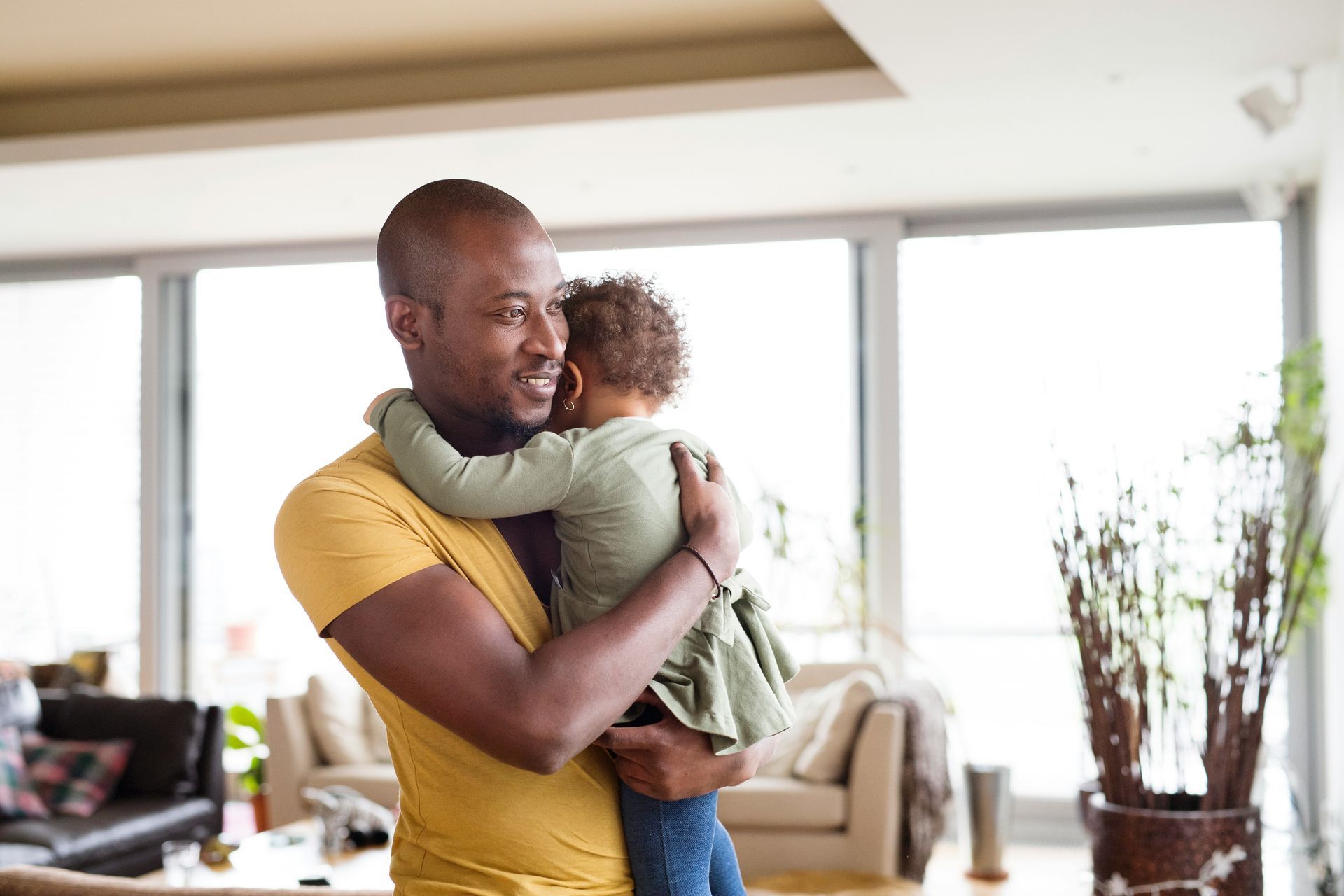 A man is holding a baby girl in his arms in a living room.