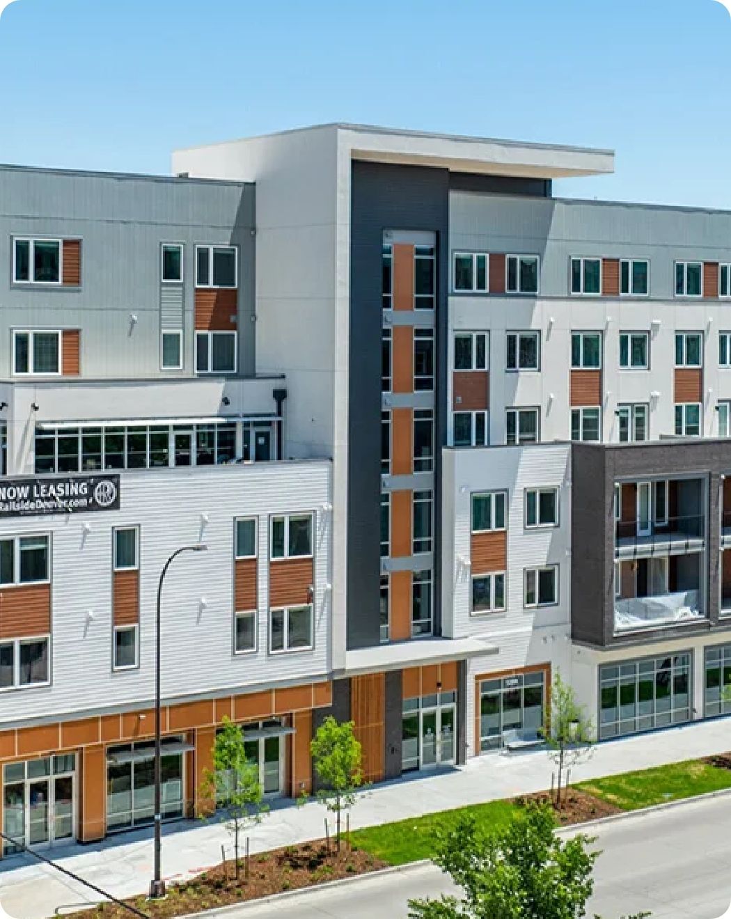 Modern multi-story apartment building with retail on the ground floor. Exterior features gray, white, and brown siding.