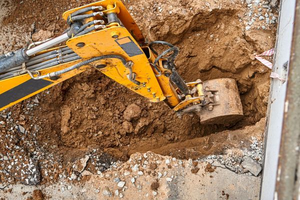 Yellow excavator digging a hole in the ground; close-up view.