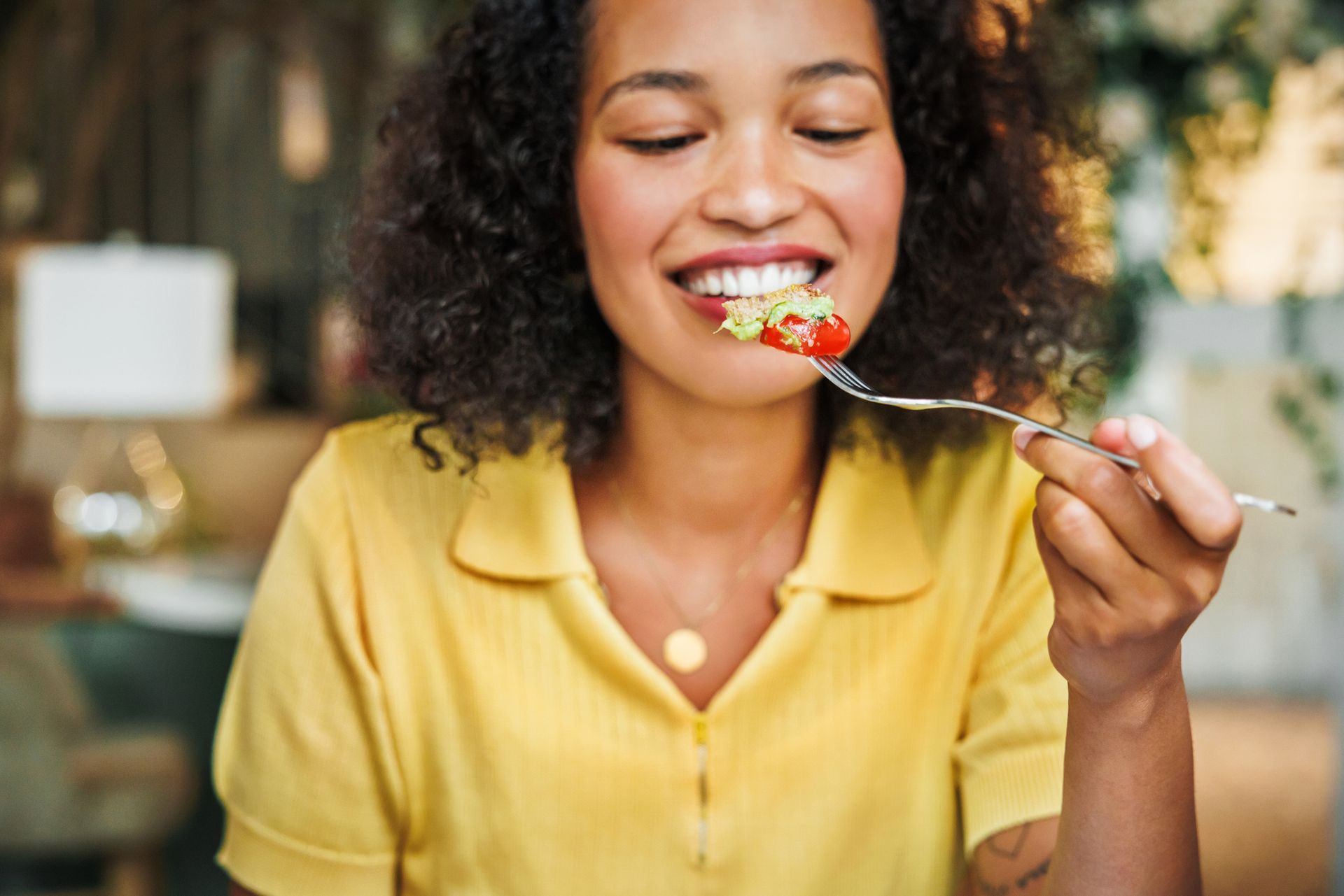 Young lady with a yellow shirt smiling about to eat tomato and salad