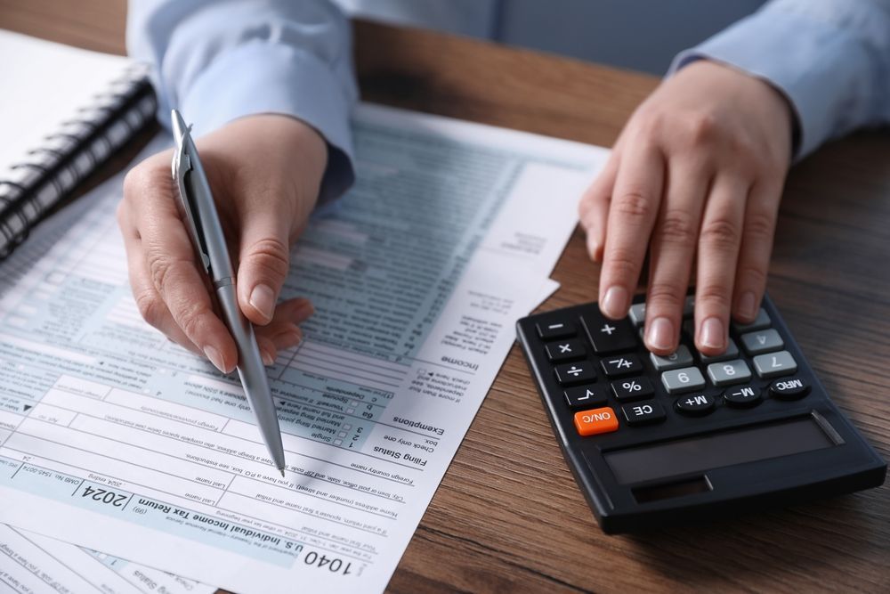 A person is using a calculator and writing on a tax form.