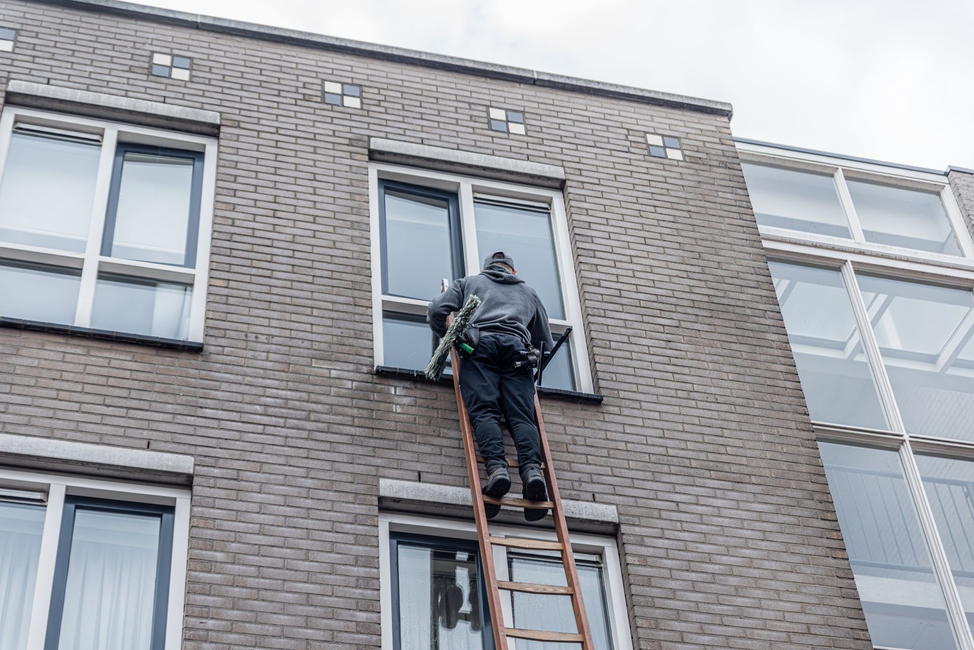 Person on a ladder cleaning a window on a brick building's exterior.
