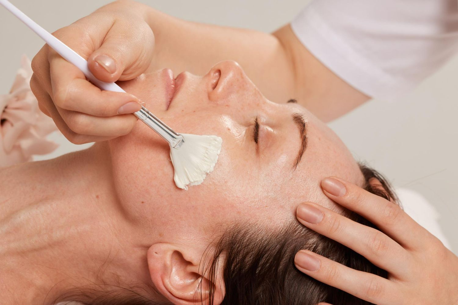 Facial treatment: A person's face being brushed with a white cosmetic product. The person is reclining.