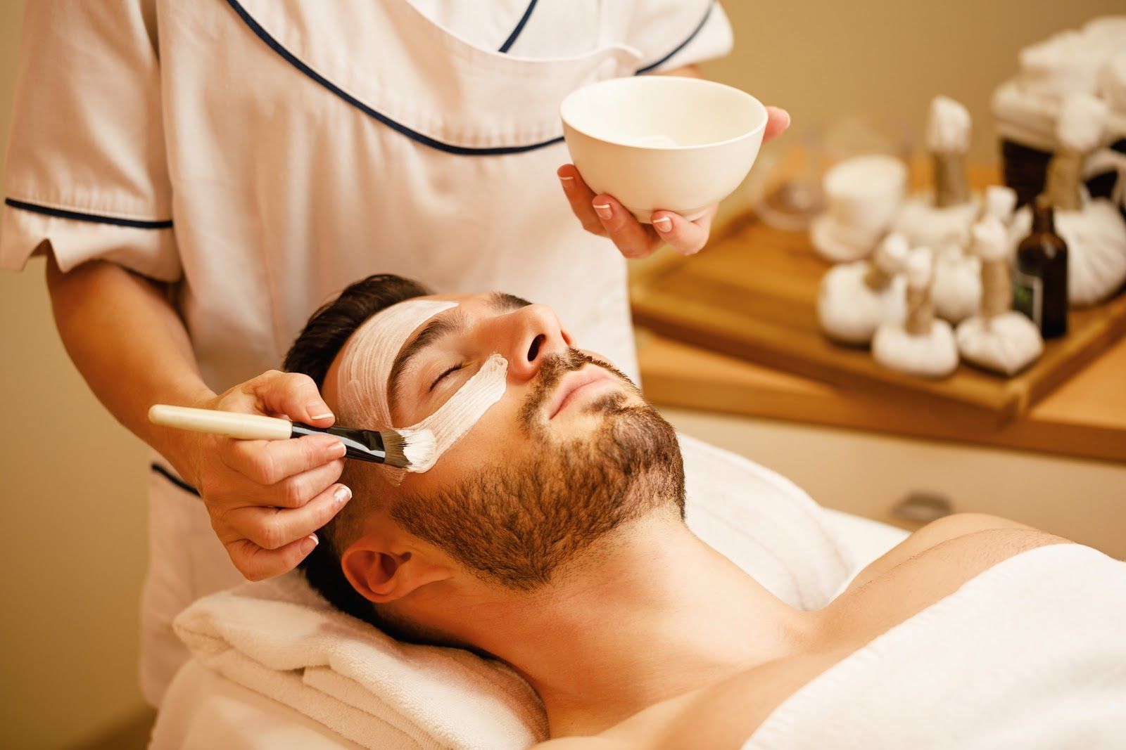Spa facial treatment with esthetician applying cream to a man’s face using a brush