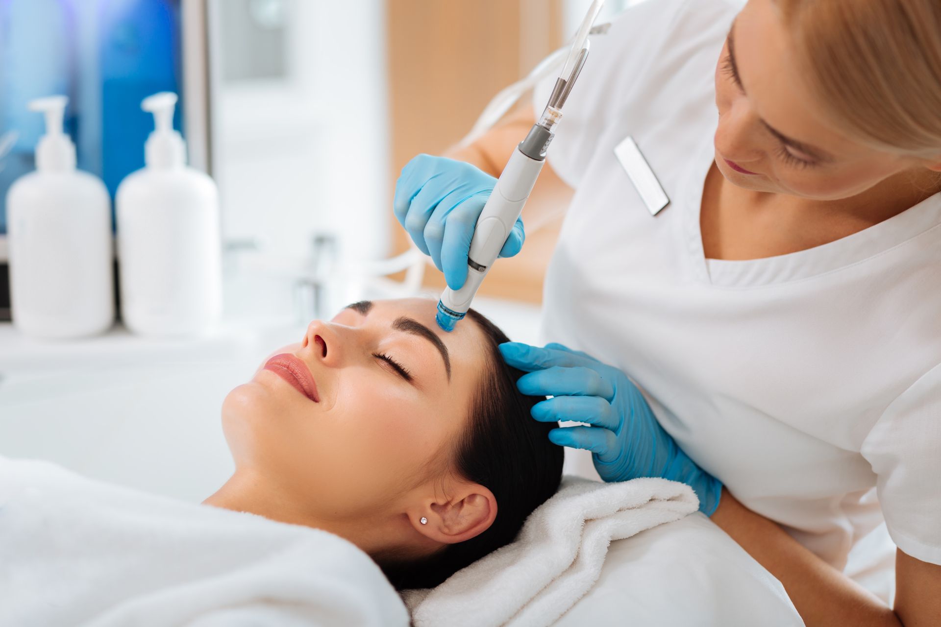 Esthetician performing a facial treatment with a device on a woman’s forehead.