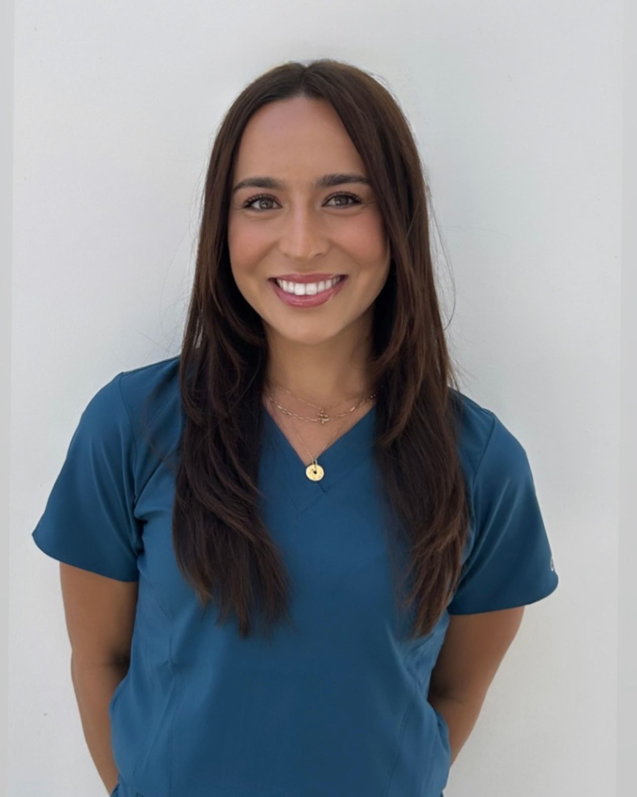 A woman in a gray scrub top and pants is smiling for the camera.