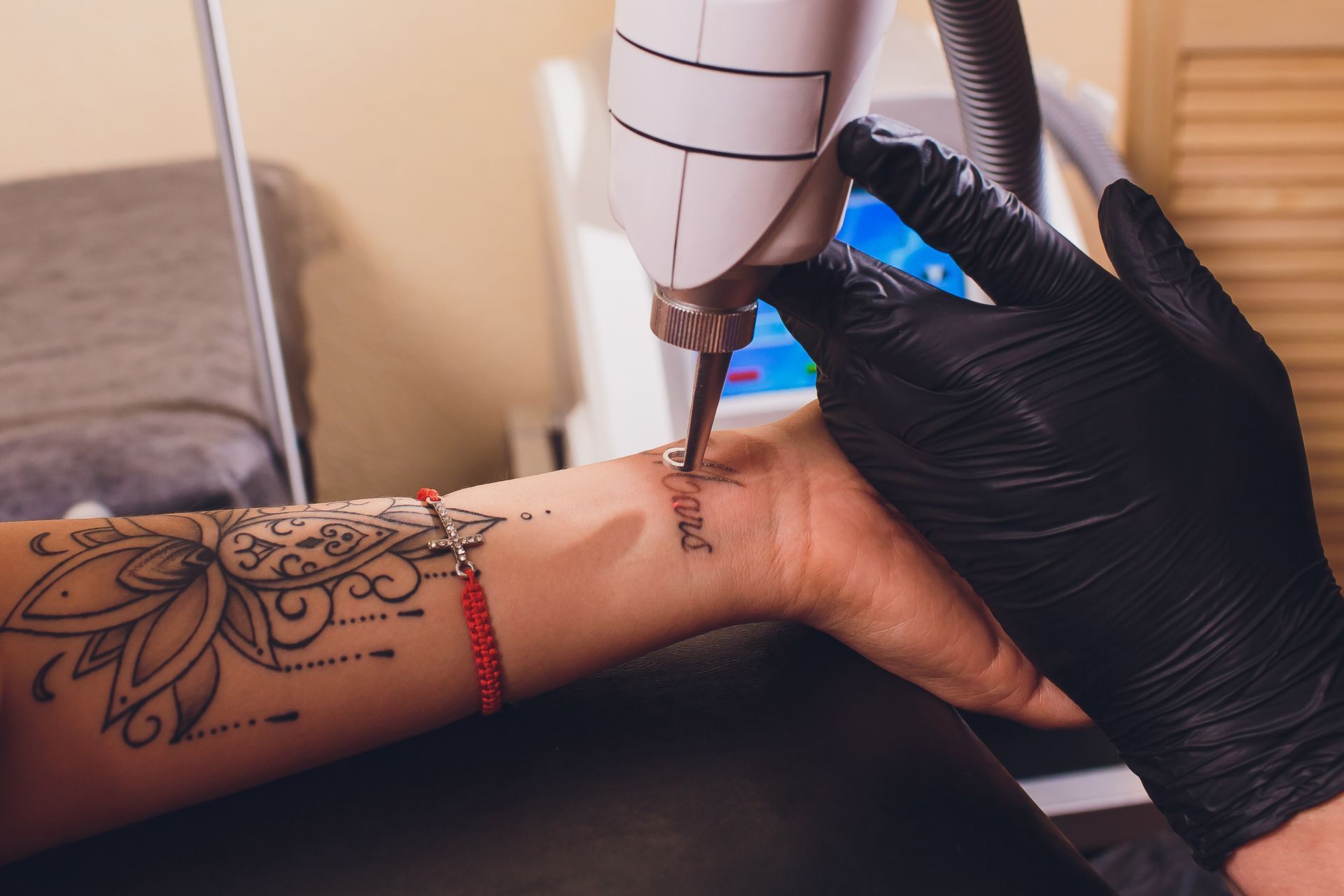 Tattoo removal treatment: A gloved hand using a laser on a wrist with existing tattoos.