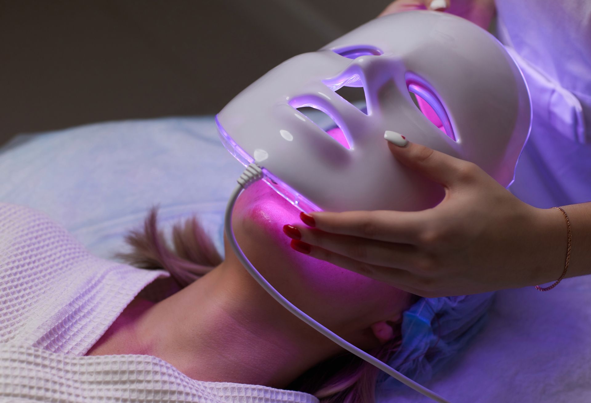 Person receiving LED light therapy treatment with a mask glowing pink, indoors.
