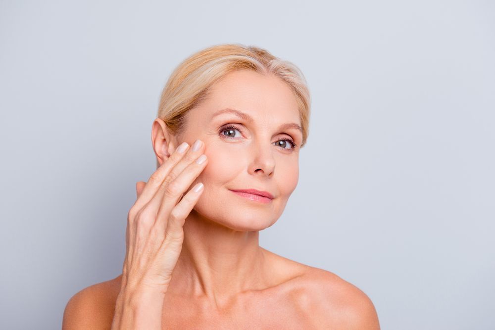 A woman is touching her face with her hand and looking at the camera.