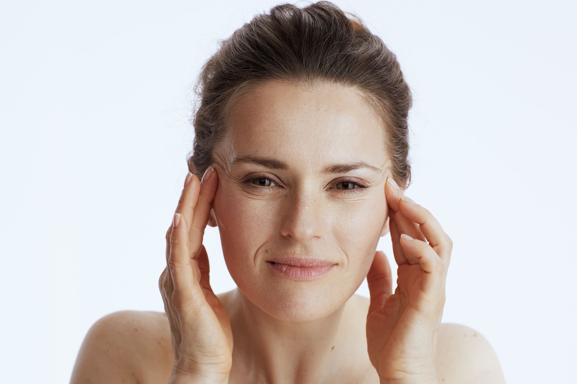 Woman gently touching her temples against a light background