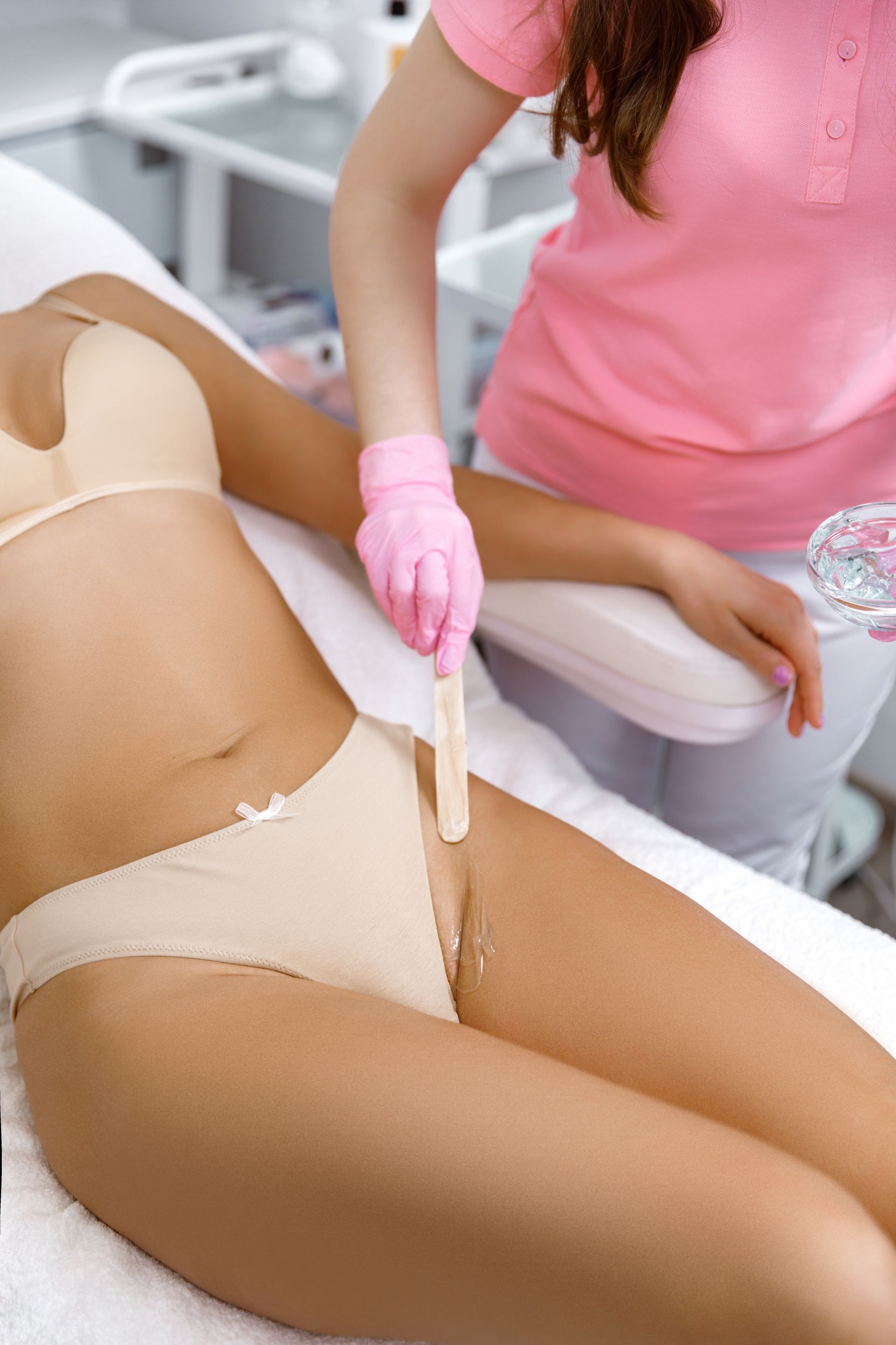 Person in pink gloves waxing a client’s bikini line in a spa treatment room