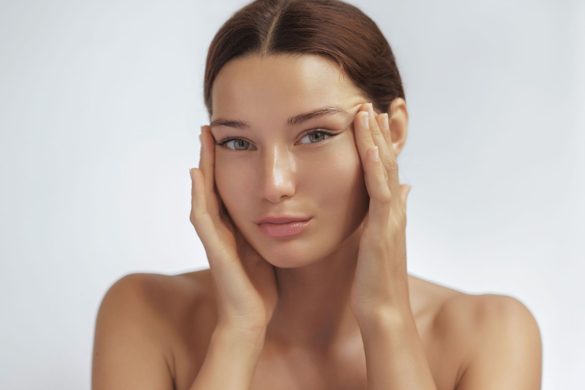 Close-up of a woman gently touching her face against a light gray background