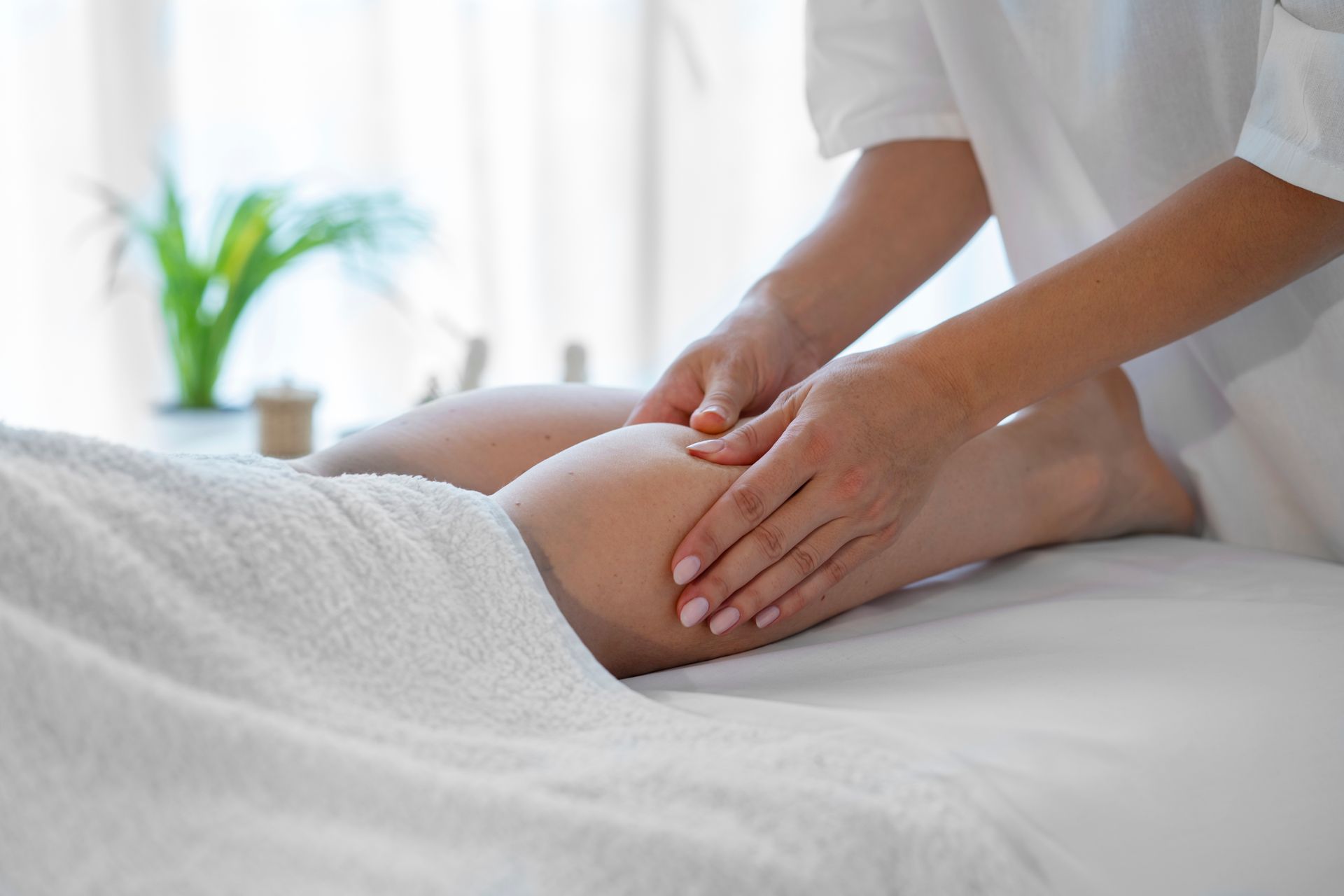 Leg receiving a massage on a white towel, hands on the calf in a bright room.