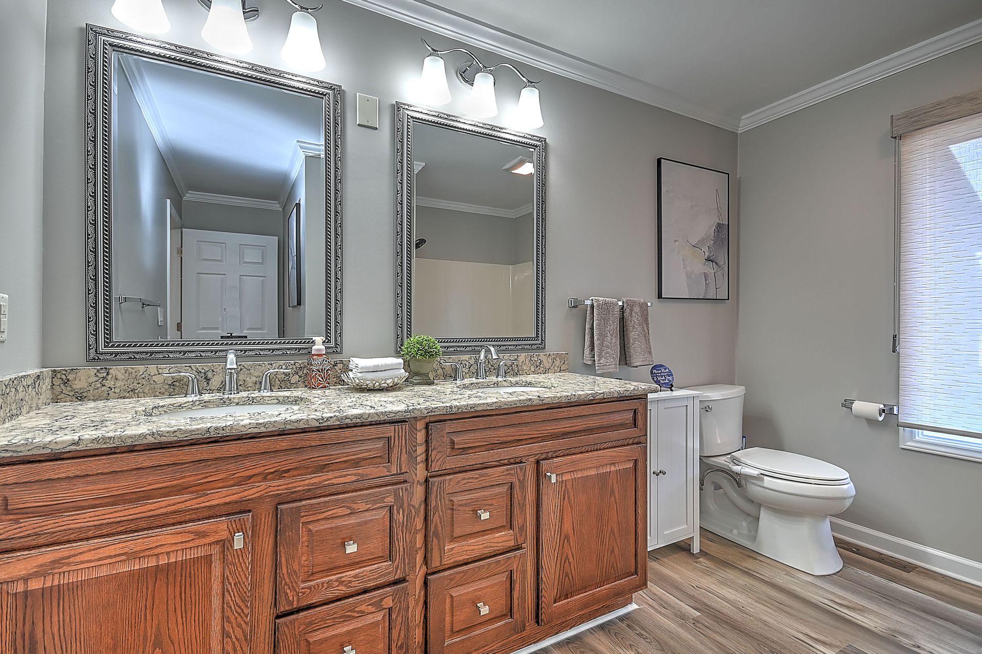 A bathroom with two sinks , two mirrors , a toilet and a window.