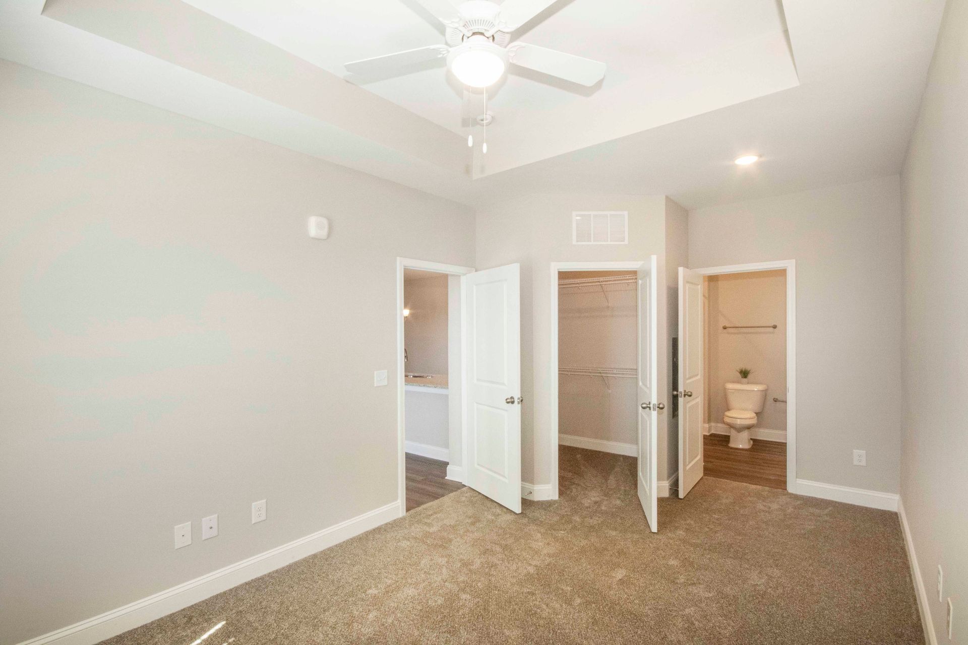 An empty bedroom with a ceiling fan and a toilet.