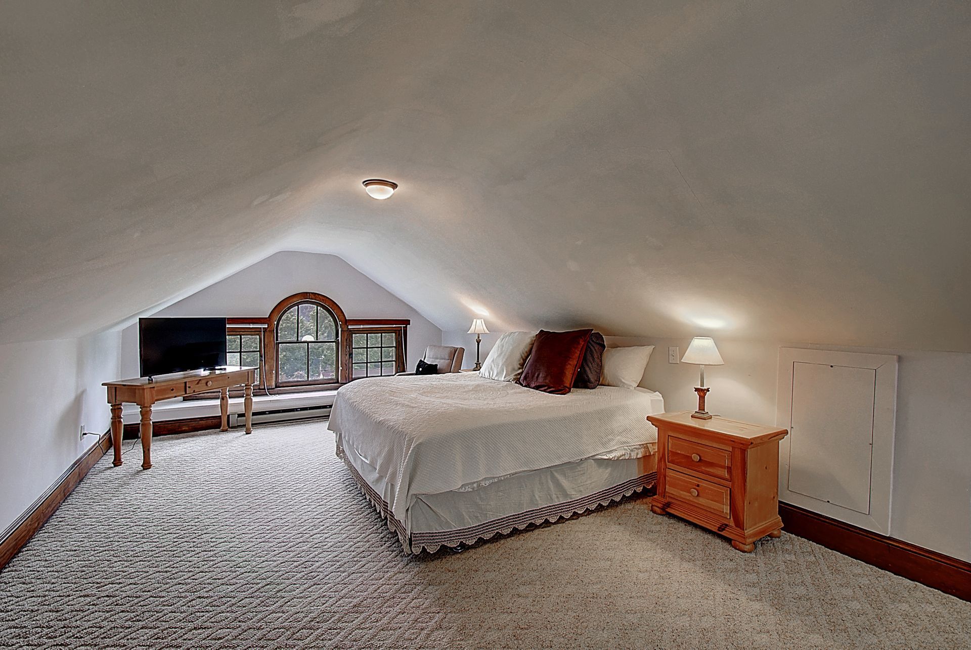 A bedroom with a king size bed , nightstand , desk and television.