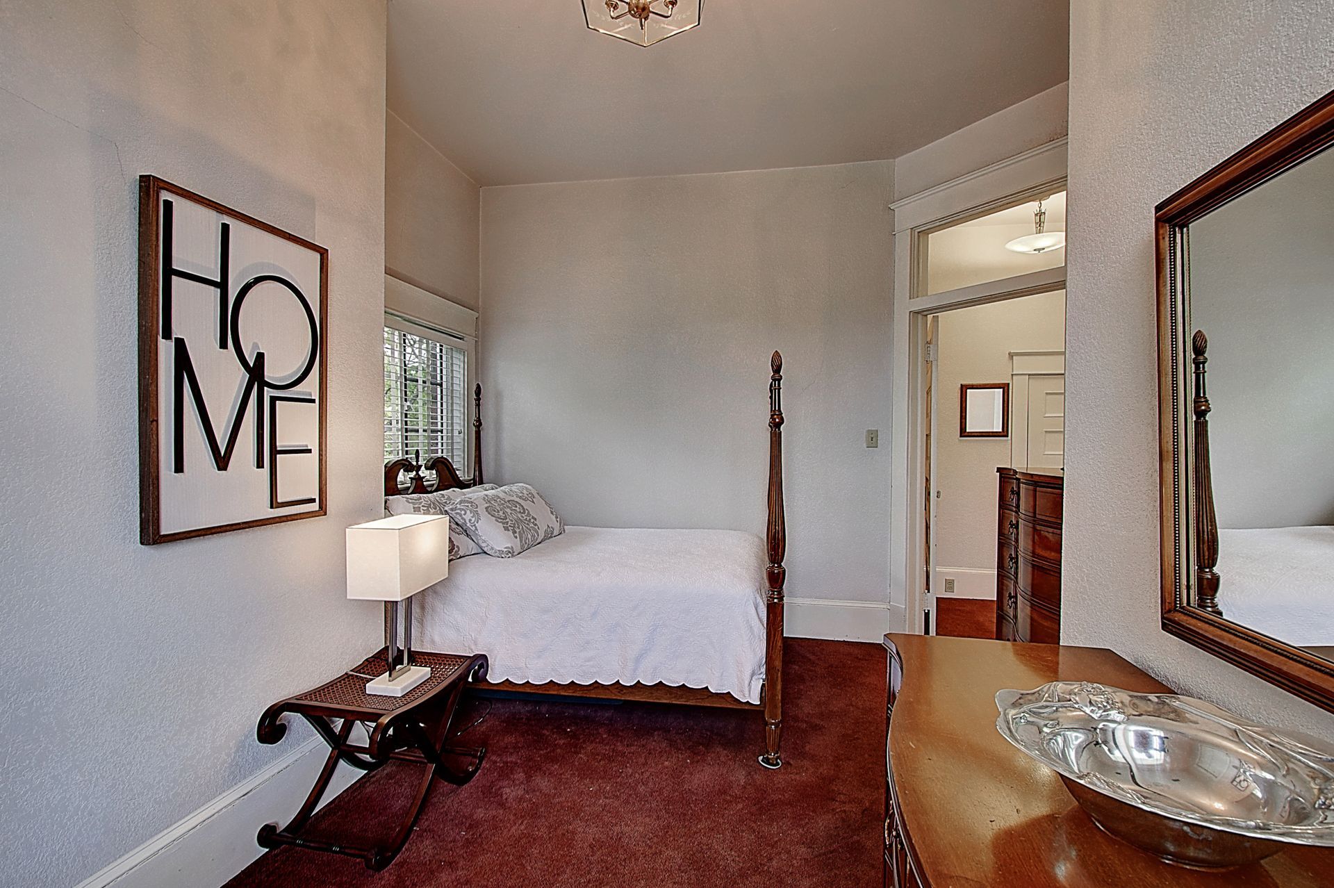 A bedroom with a bed , dresser , mirror and a sign that says home on the wall.