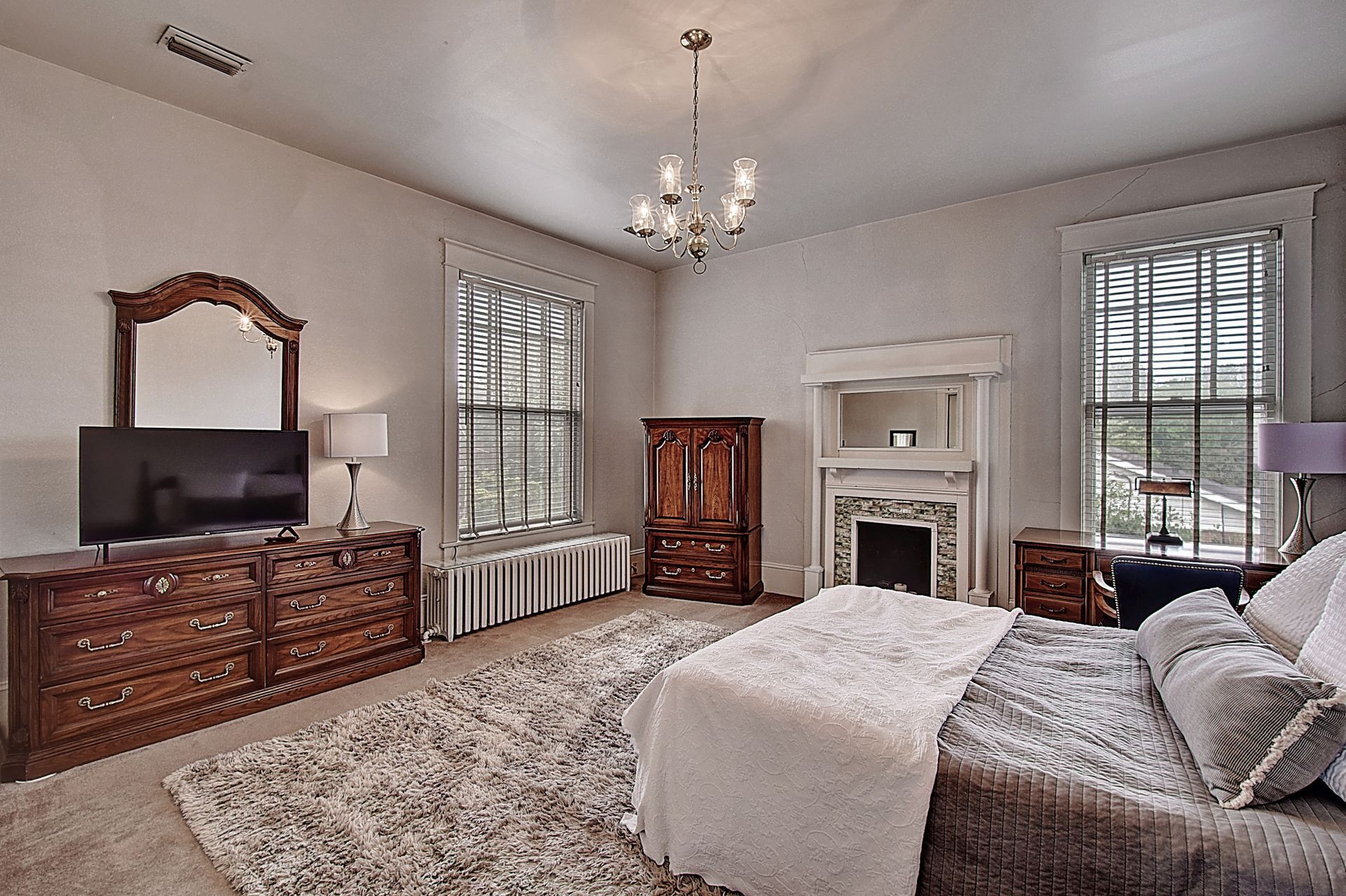 A bedroom with a bed , dresser , television and fireplace