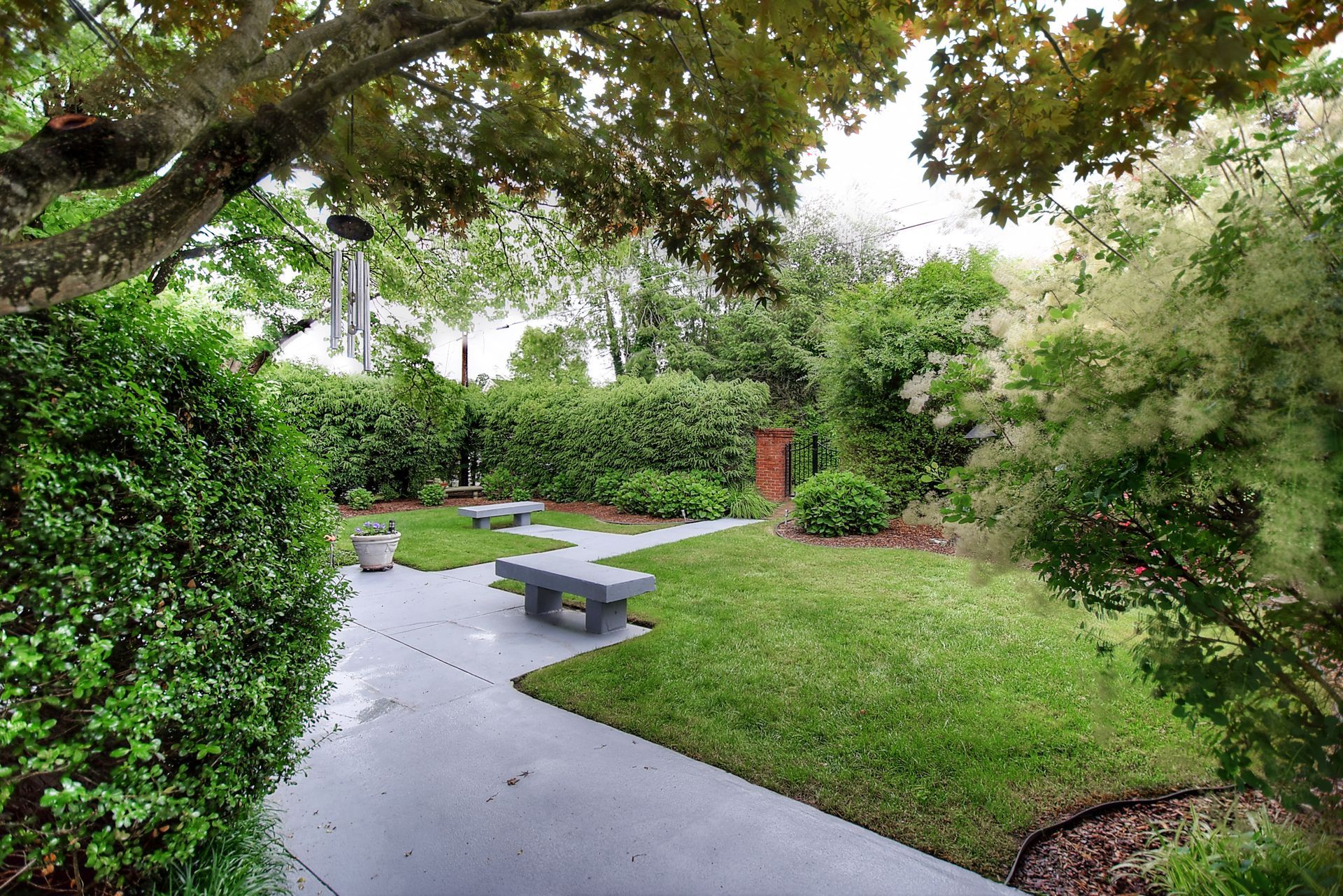 A park with a concrete walkway and benches surrounded by trees and bushes.