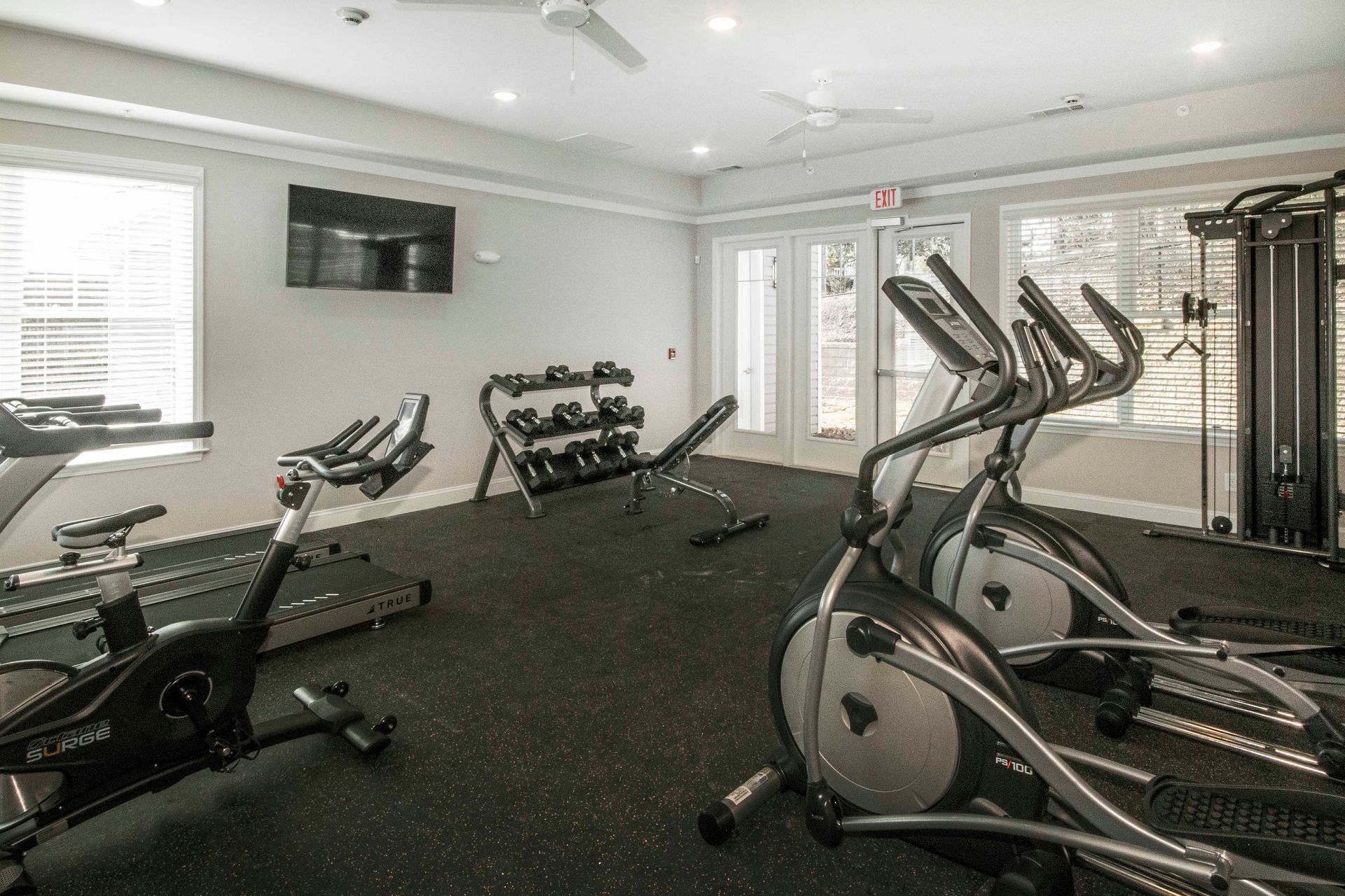 A gym with a lot of exercise equipment and a television on the wall.