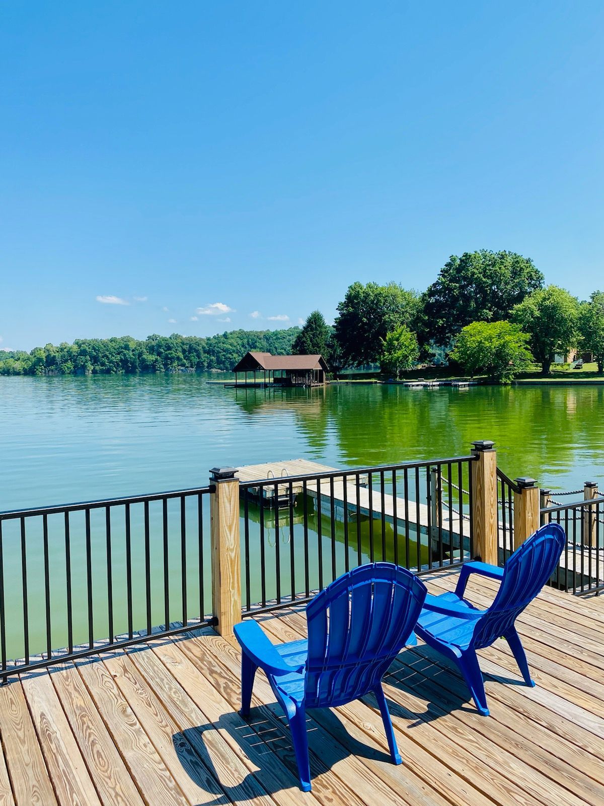 Two blue chairs are sitting on a wooden deck overlooking a lake.