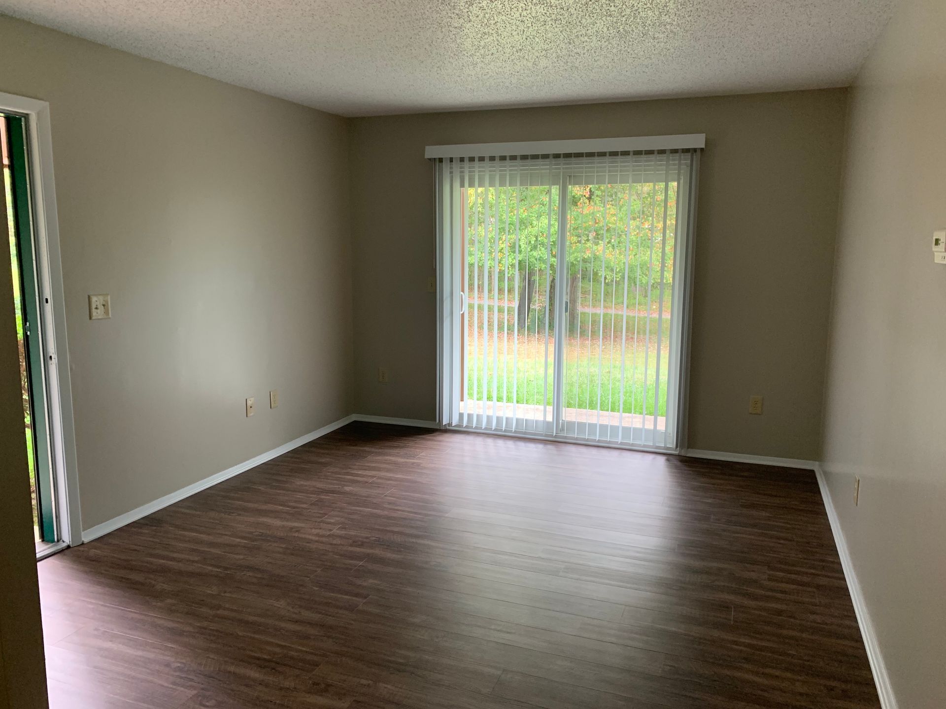 An empty living room with a sliding glass door and hardwood floors.