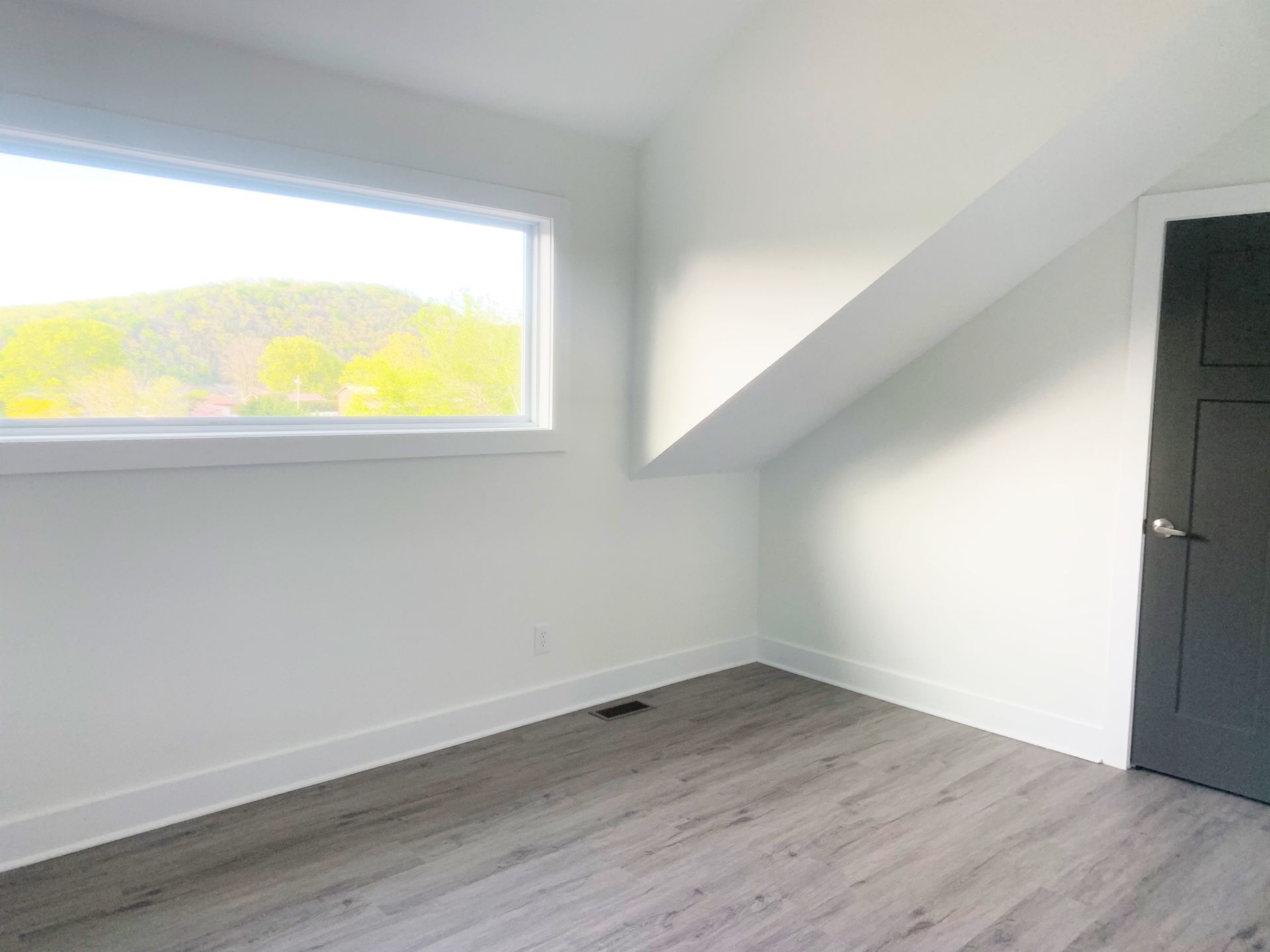 An empty room with a window and a black door.
