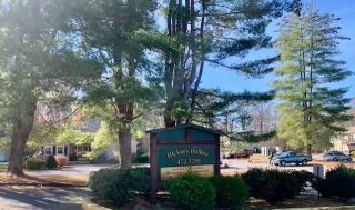 A sign in front of a house in a residential area surrounded by trees.