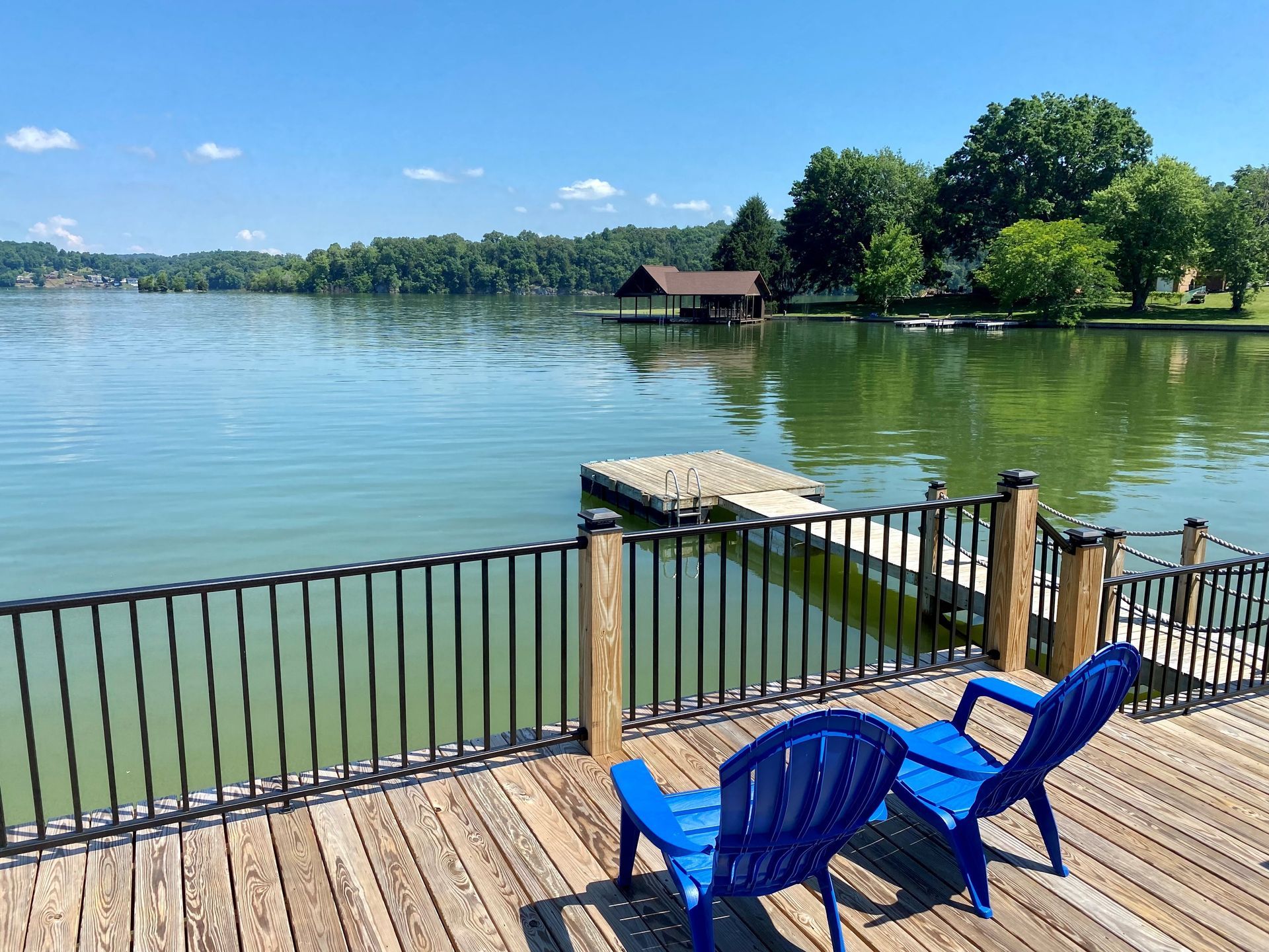 Two blue chairs are sitting on a wooden deck overlooking a lake.