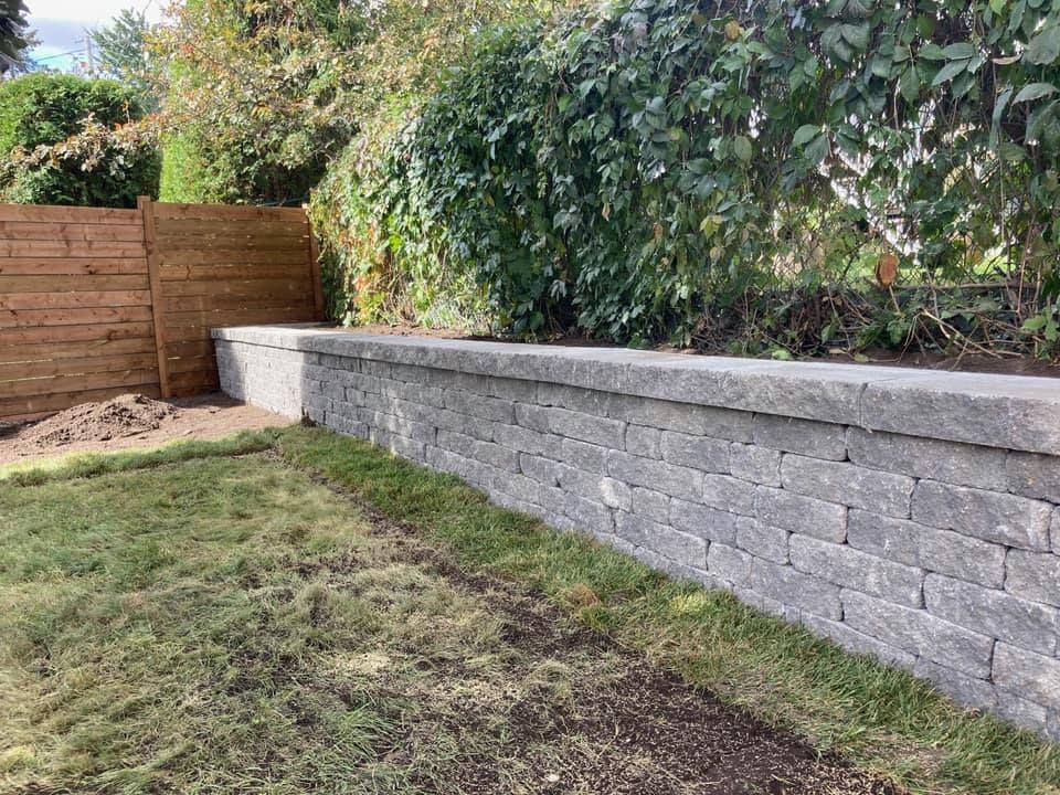 Un mur de pierre dans une cour arrière à côté d'une clôture en bois.