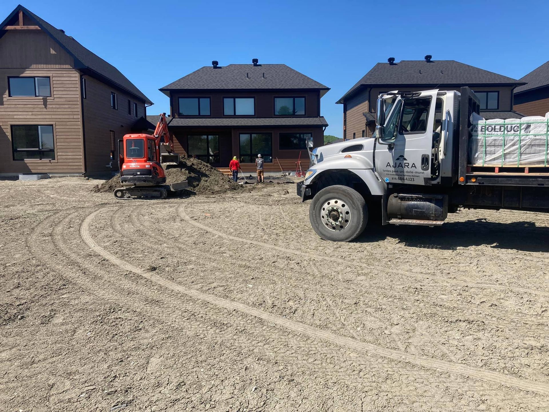 Un camion est garé dans un champ de terre devant une maison.