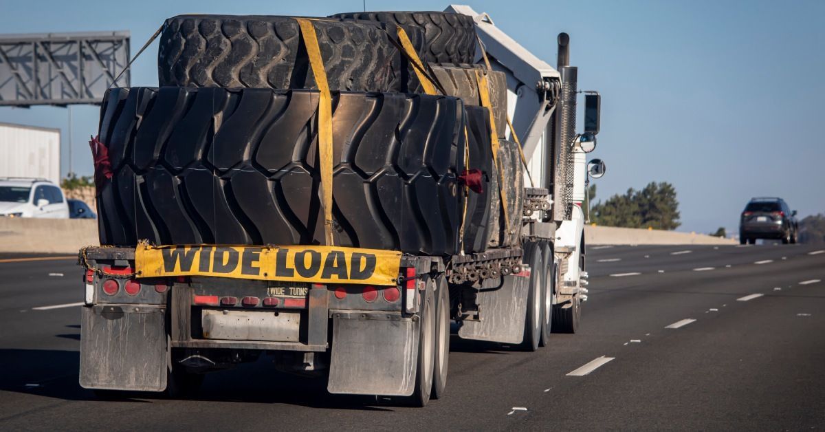 Stacks of large tires tied down to a flatbed with a “wide load” sign are being transported on the highway.
