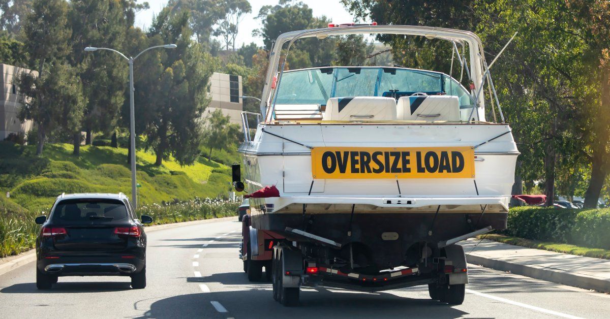 A truck carries a large, white boat on the back of its trailer with a banner that says 