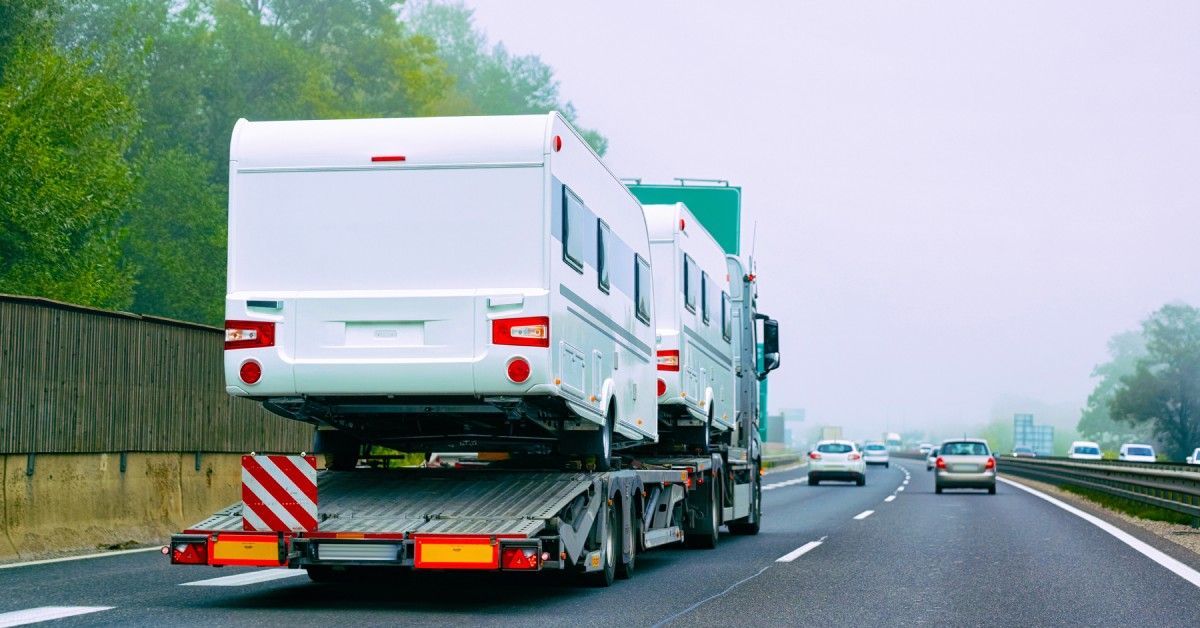 A transport flat-bed truck, hauling motor homes. Other vehicles are passing the truck on the highway