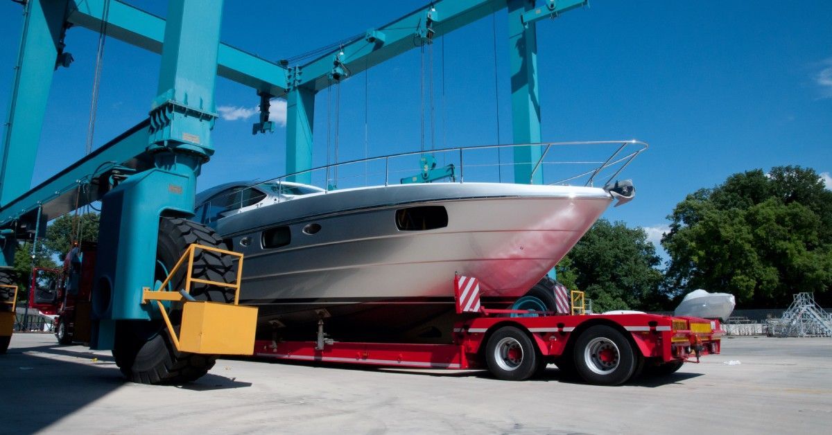 A large crane system surrounds a yacht on top of a red trailer. The crane is either lifting the vessel off or onto the trailer.
