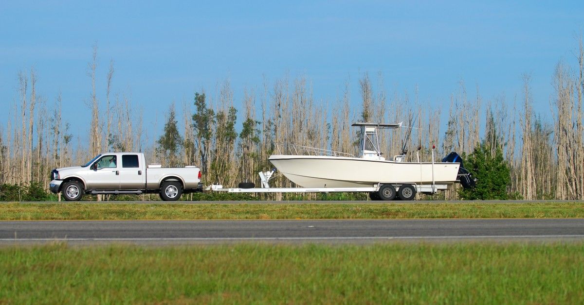 A semi truck with a large boat covered in white shrink wrap on the back of the trailer.