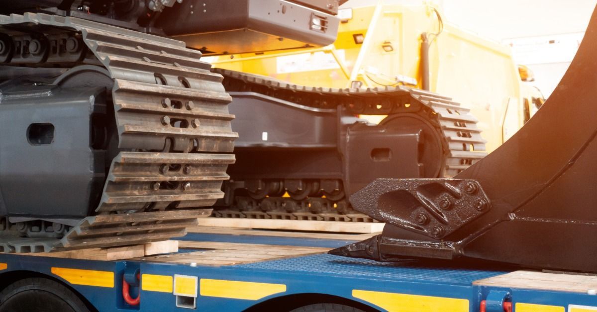 A close-up of a construction machine positioned on a flatbed trailer. The tracks on the equipment rest on some two-by-fours.