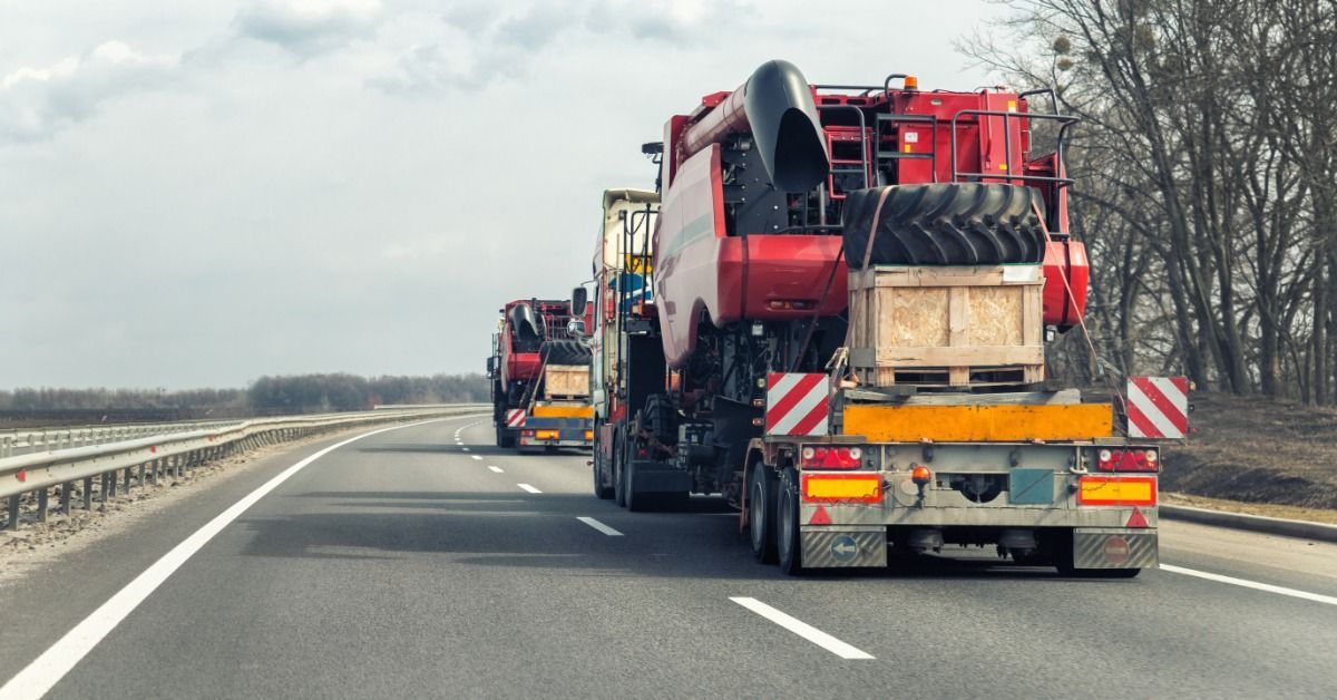 Two semi trucks drive down a road with large, red construction equipment.