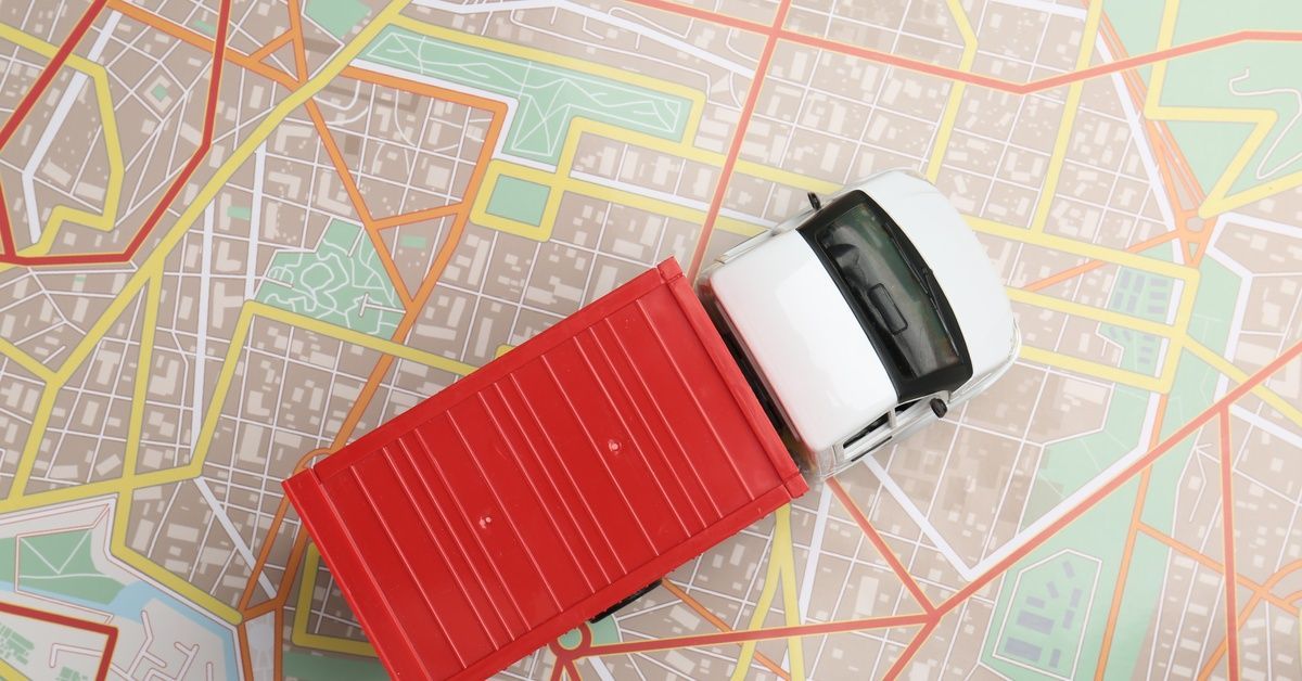 A toy truck with a red trailer rests on a city map, where white, red, orange, and yellow routes mark different paths.