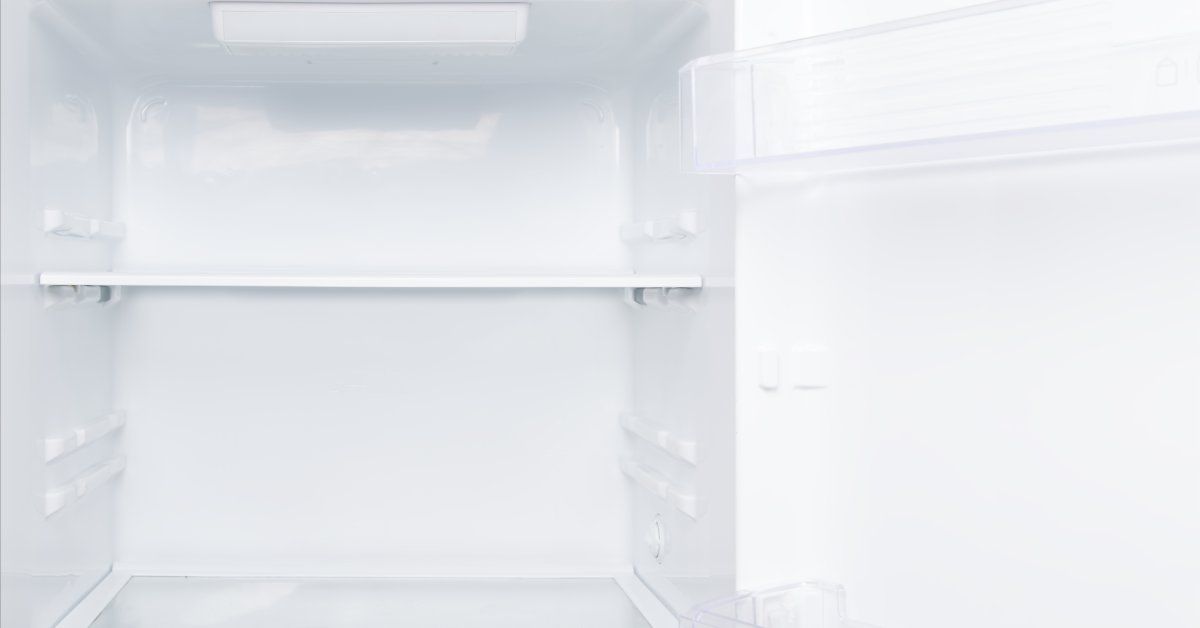 An open white refrigerator revealing two empty shelves inside with two more empty shelves on the door.