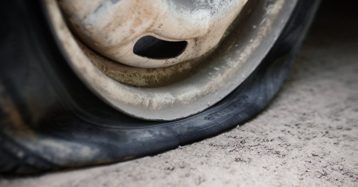 A close-up of a flat tire mounted on a metal rim with visible oxidation and surface discoloration.