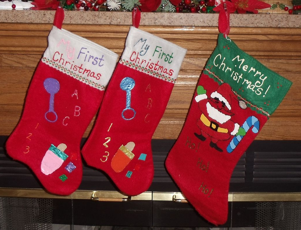 Three red Christmas stockings hanging on a mantle, embroidered with 