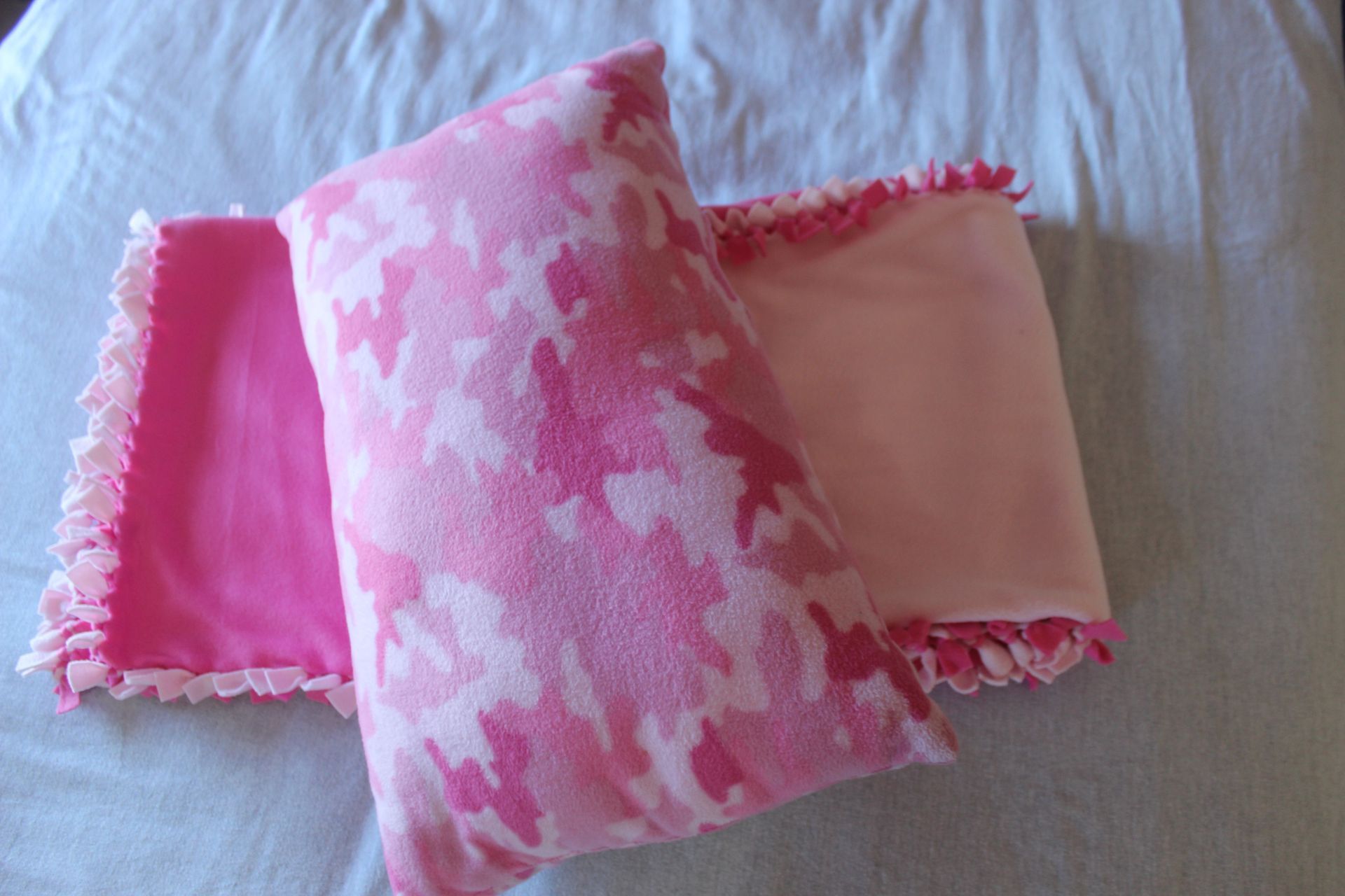 Pink fleece pillows and blanket with fringed edges.