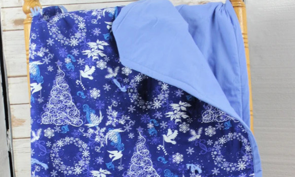 Blue Christmas blanket with a festive pattern, folded over a wooden chair.