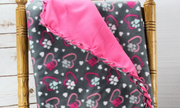 Fleece blanket, gray with pink hearts and paw prints, folded over a wooden chair, pink inside.