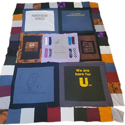 Quilt made of various t-shirts, featuring phrases and designs in a patchwork pattern, with colorful borders.