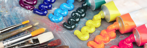 Paint tubes squeezing colorful paint onto a surface, with paintbrushes nearby.