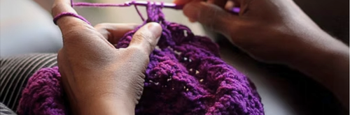 Hands crocheting with purple yarn and a hook.