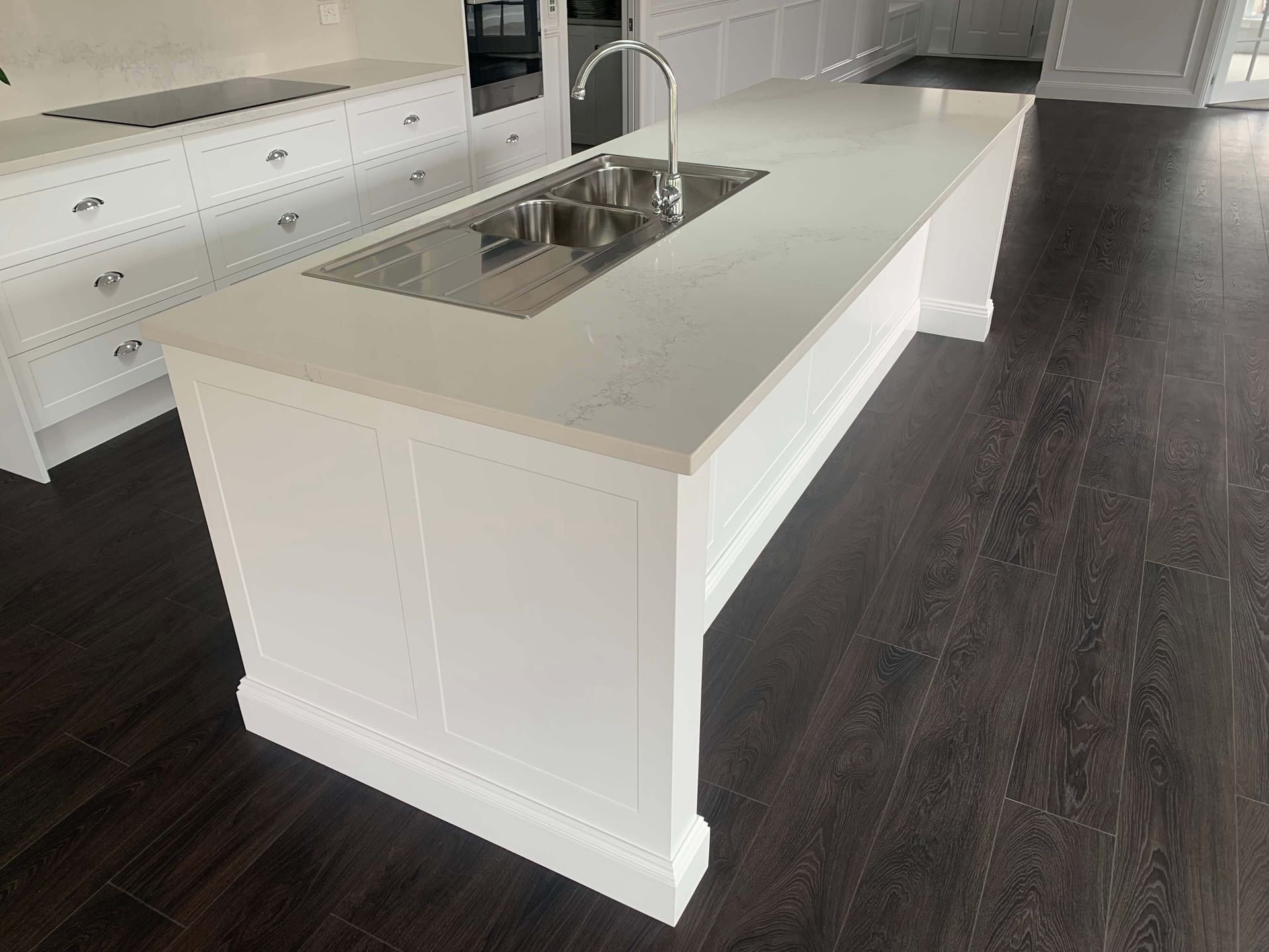 A kitchen with white cabinets and a large island with a sink.