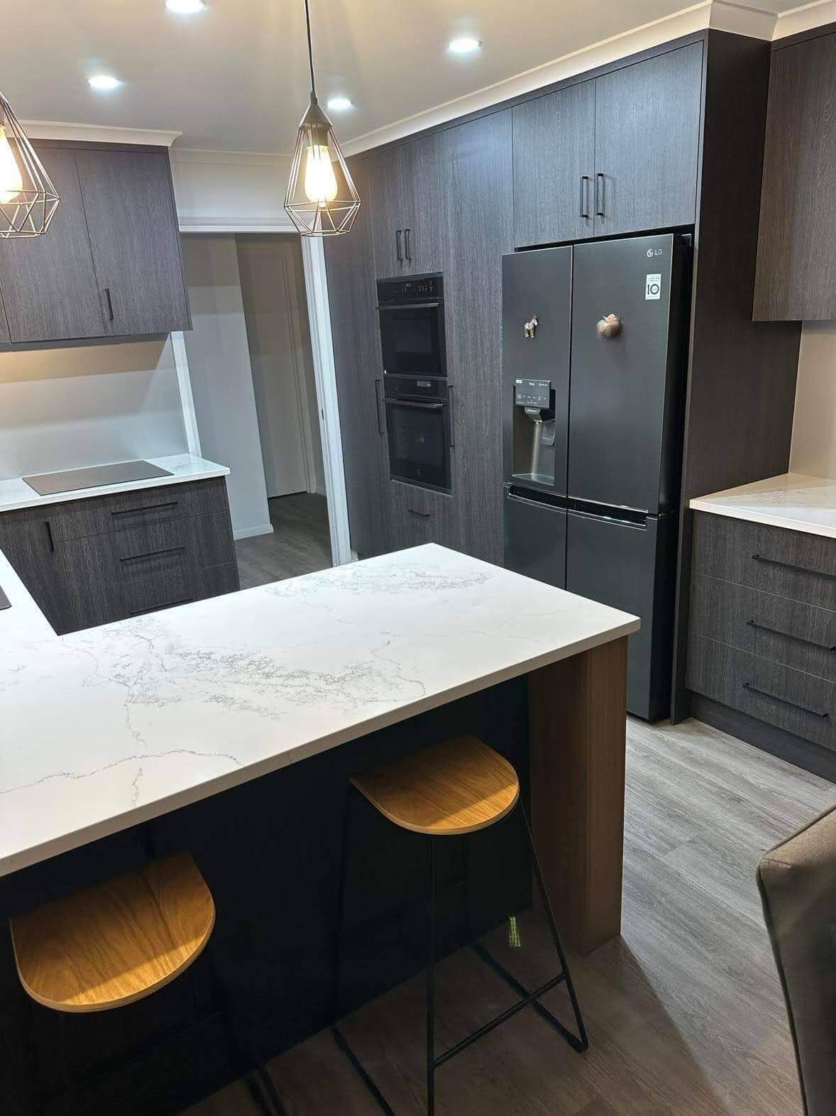 A kitchen with a large island, stools , a refrigerator and a microwave.